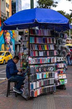 A vibrant street vendor booth in Bogotá selling various phone accessories under a large umbrella.