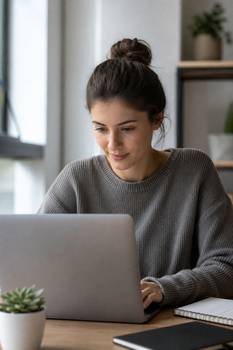 A young woman focused on her laptop, studying in a modern indoor setting.