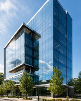 Contemporary glass-fronted office building with trees in urban setting on a sunny day.