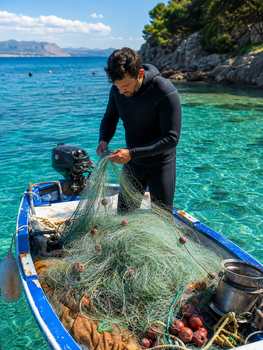 Fisherman in a wetsuit arranging nets on a boat in clear waters. Perfect for marine and fishing themes.
