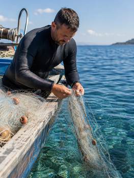 Fisherman in a wetsuit arranging nets on a boat in clear waters. Perfect for marine and fishing themes.