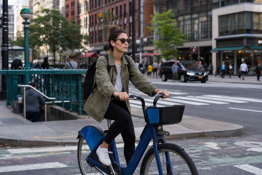 Woman rides Citi Bike near New York's 23rd Street Station, embracing urban lifestyle.